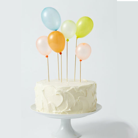 White icing cake on top of a white cake stand. Small balloons placed as cake toppers.