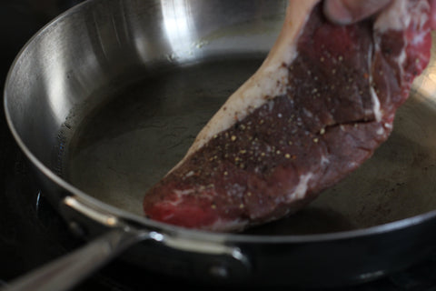gently placing raw steak onto hot pan