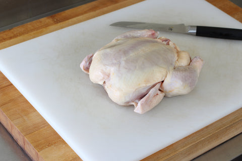 whole raw chicken on cutting board with boning knife