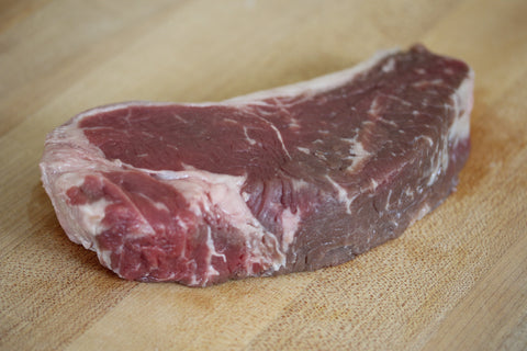 raw new york steak on wooden cutting board