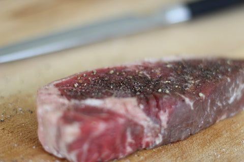 seasoned raw new york steak with salt and pepper on cutting board