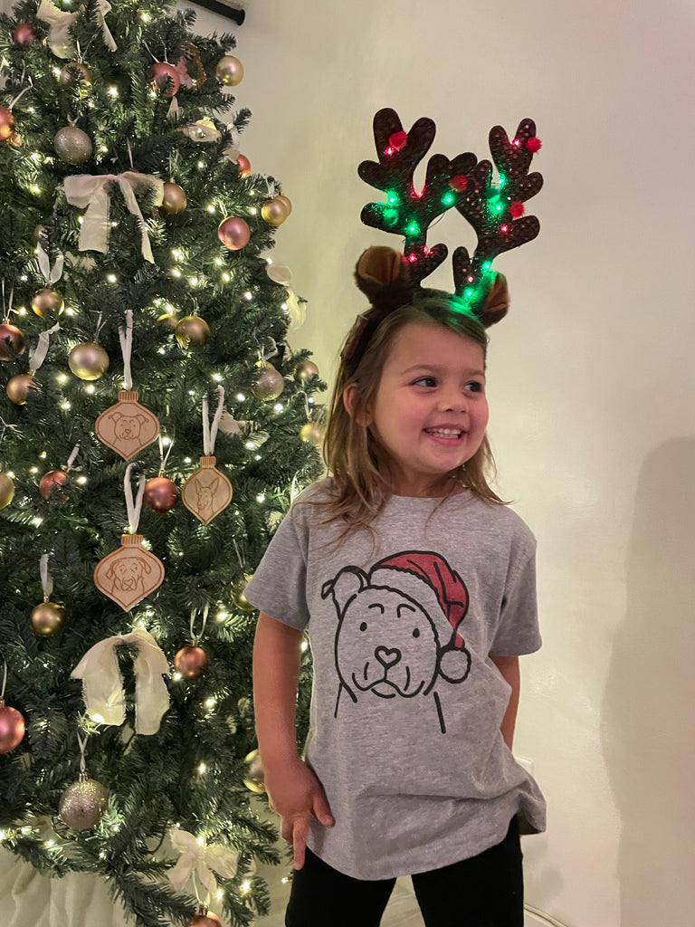 Child wearing Christmas shirt with a dog wearing a Santa hat
