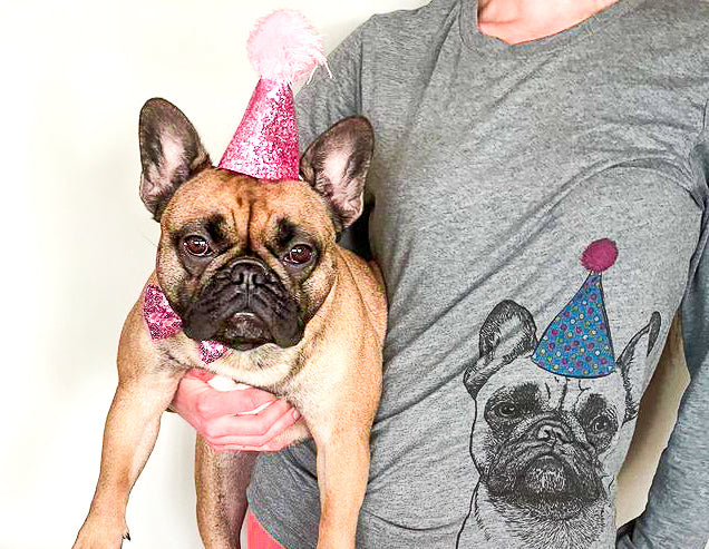 girl wearing dog shirt with birthday hat holding a dog with a birthday hat