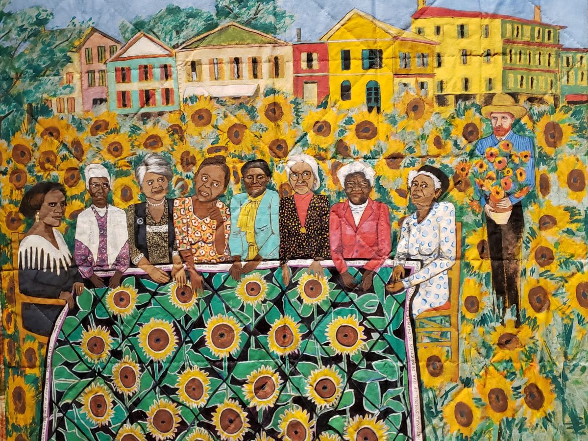 Pintura sobre colcha de mujeres negras activistas que sostienen una colcha de girasoles en un campo de girasoles