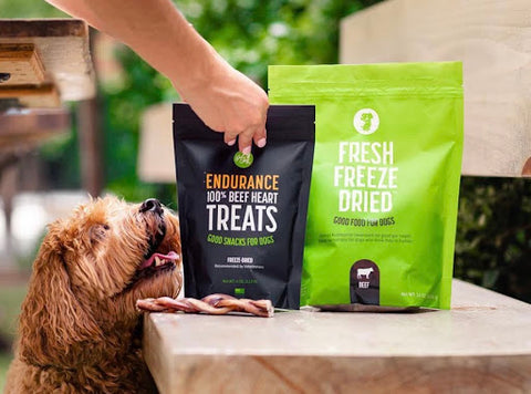 A dog looks up hungrily at Get Joy Freeze Dried Treats that their owner is putting on a table. 