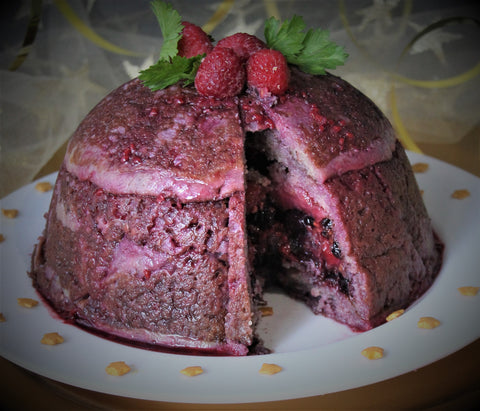 Dessert made of a dome of pancakes soaked in berry juice and stuffed with raspberries, blackberries, blueberries and strawberries. The dome has a slice removed so you can see the filling. With bright red freeze dried and frozen raspberries and green leaves on top.