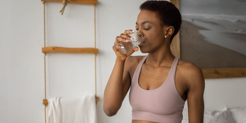 Woman in workout clothing drinking glass of water | IMportance of Hydration in a woman’s wellness routine