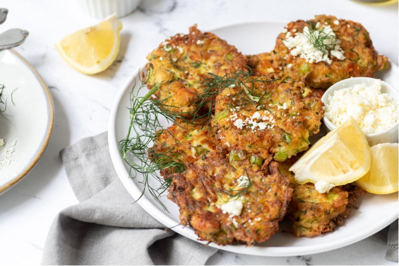 Zucchini patties plated beautifully with a side of lemon wedges and feta cheese.