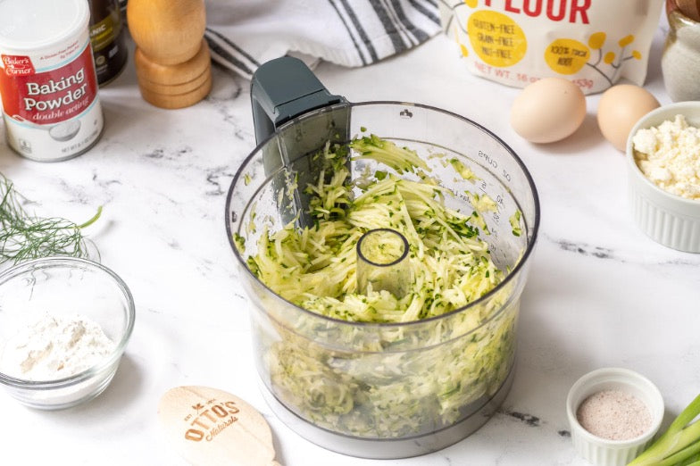 A food processor with chopped up zucchini inside.