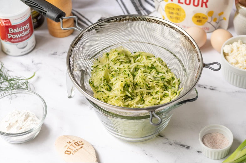 Grated Zucchini being strained through a thin strainer over a measuring cup.