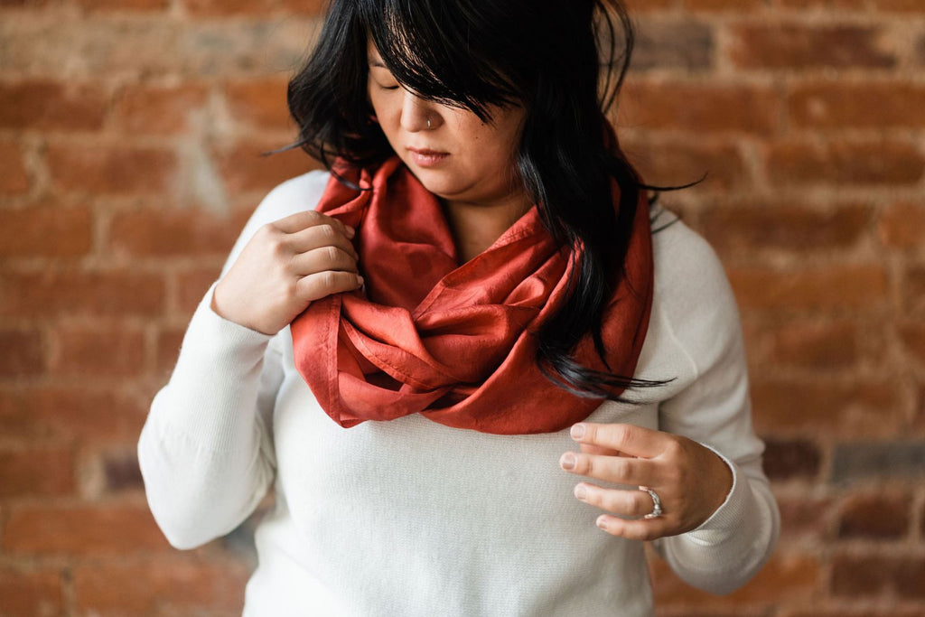 Chinese American woman with long, wavy hair, wearing a white pullover sweater and Russet red silk infinity scarf that is 22 by 76 inches