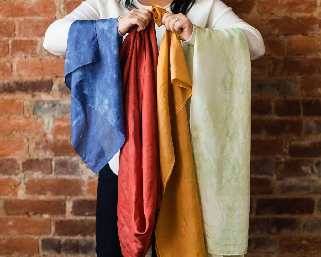 Cropped photo of woman holding an array of colorful silk scarves in front of her, draped over her arms.