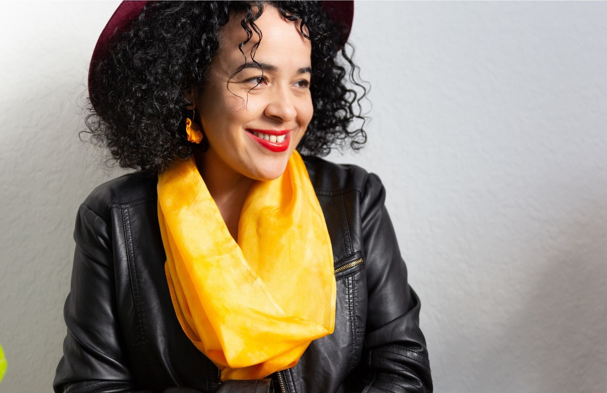 Black woman with curly hair wearing a red hat, leather jacket and silk scarf in Bright Topaz