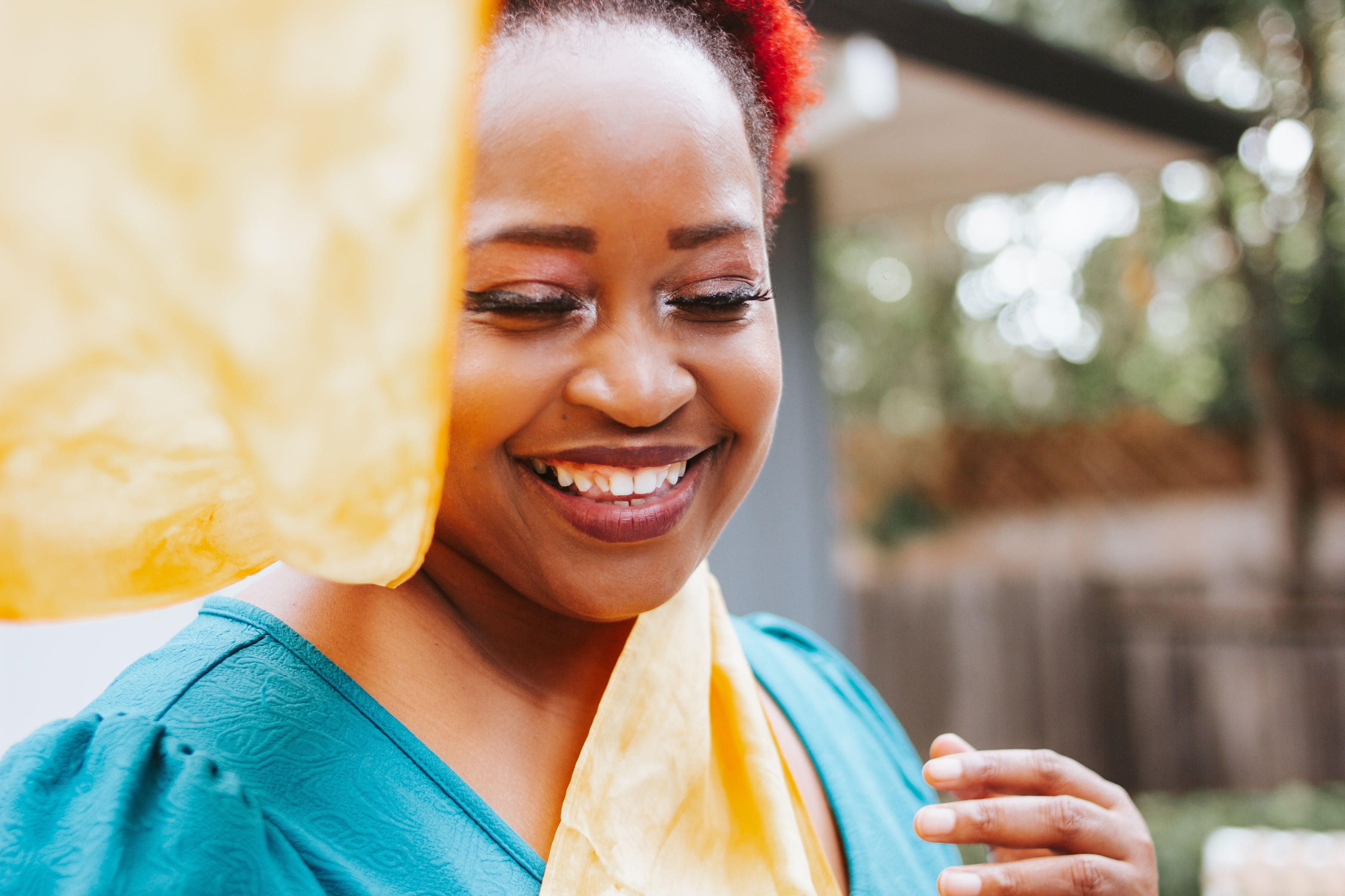 black woman wearing yellow silk scarf, one end tossed in the air in front of her