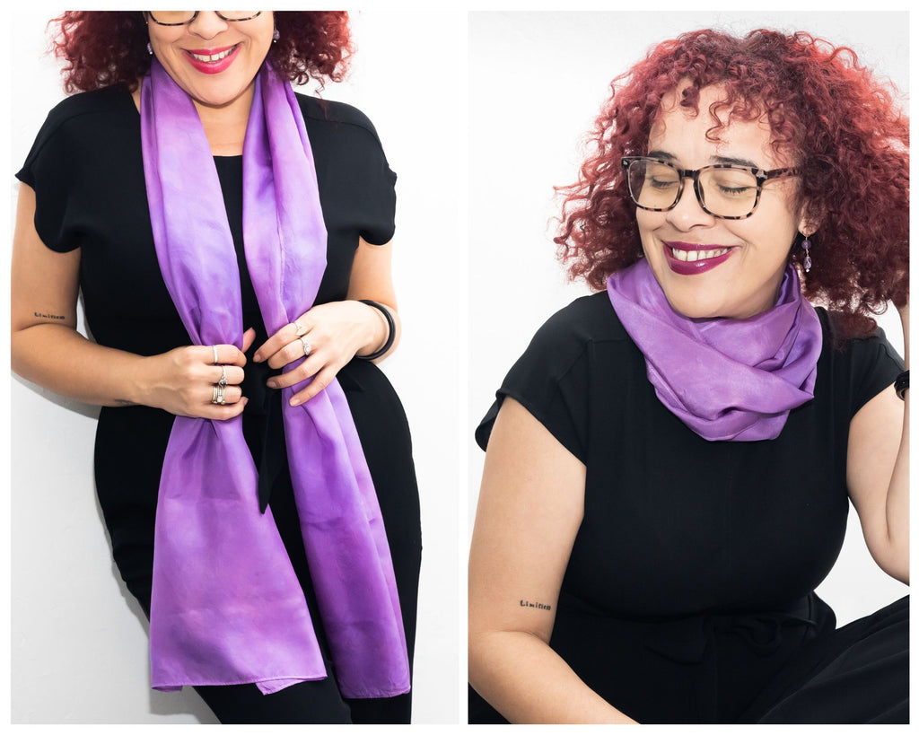 Two photos of an Afro Cubano woman with shoulder length, loosely coiled black hair tinted red and thick rimmed glasses, wearing a black t shirt and black jeans.  She has a long crocus purple silk scarf draped over her shoulders in one photo and wrapped closely around her neck in the other photo.