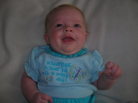 Photo of Katie's first smile at 2 months old with a light blue shirt that reads "Butterflies flutter by on a lovely day"