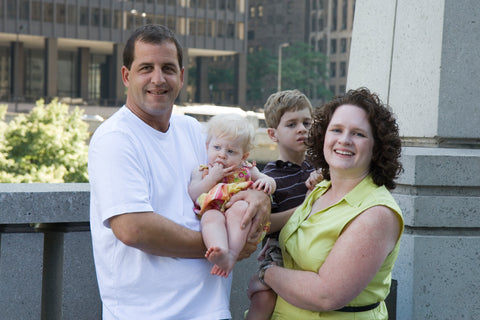 Picture of a family. Dad is holding a baby girl and mom is holding a young boy. 