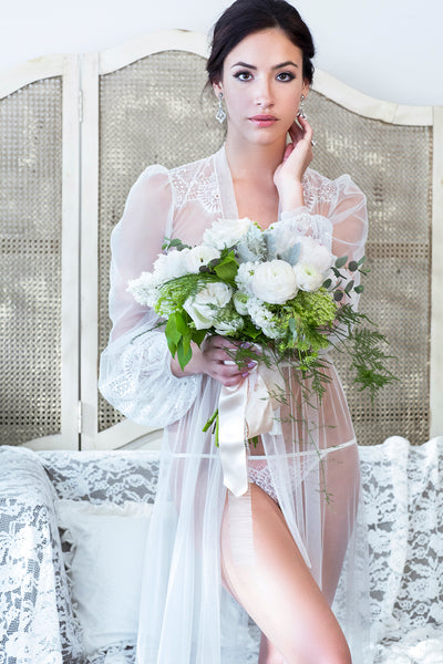 Bride on her wedding morning in a sheer white dressing gown with vintage style lace applique and bouquet