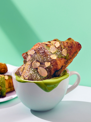 A croissant stuffed with matcha frangipane and topped with sliced almonds dunked in a matcha latte