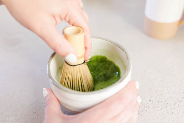 Mixing matcha with a traditional bamboo matcha whisk in a white matcha bowl