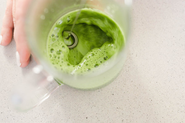 Mixing matcha in a clear glass with an electric milk frother