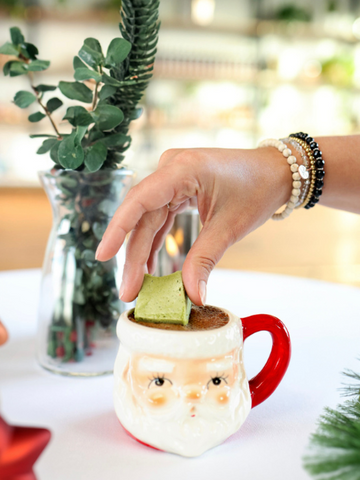 santa mug filled with hot cocoa and a hand adding a matcha marshmallow