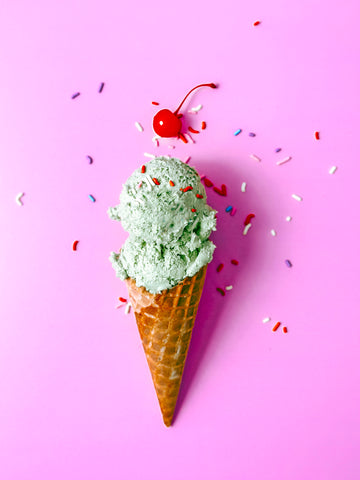 Matcha Nice Cream in a Waffle Cone on a pink background with sprinkles and a cherry on top