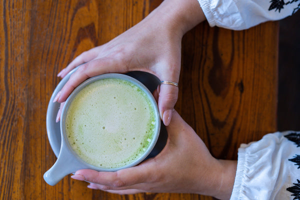 Hands around a grey mug of matcha latte on a wooden table