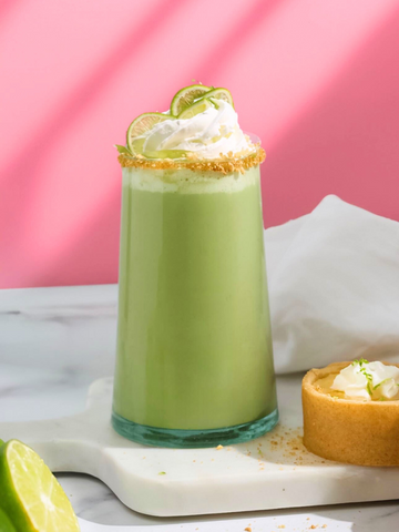 Key lime pie matcha latte with a pink and white background and an actual key lime pie on a table.