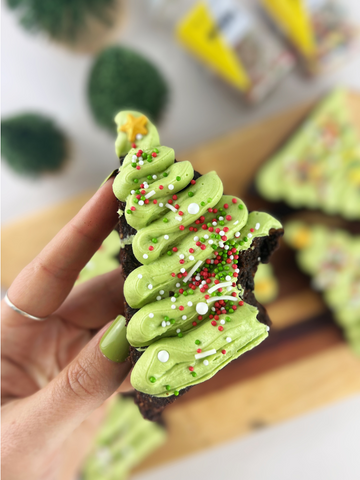 A brownie cut into a triangle with green frosting and sprinkles to make it look like a christmas tree