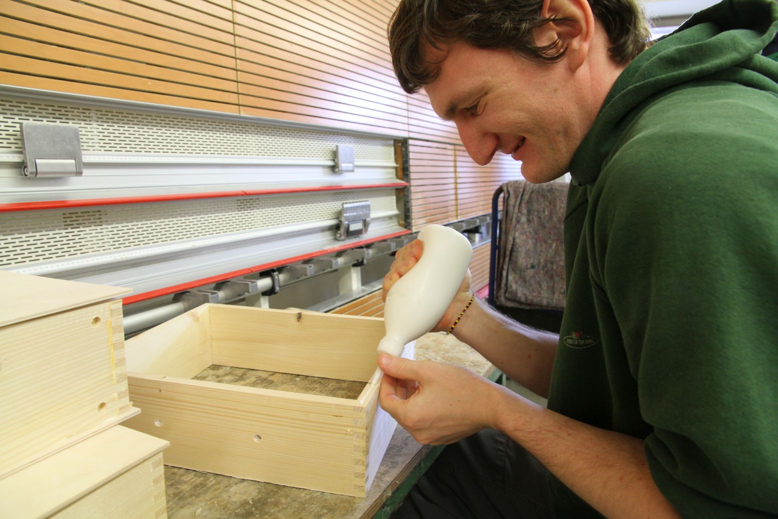 A man at a workshop for skilled workers with disabilities glues a wood box for Metalog's collection of sustainable training tools