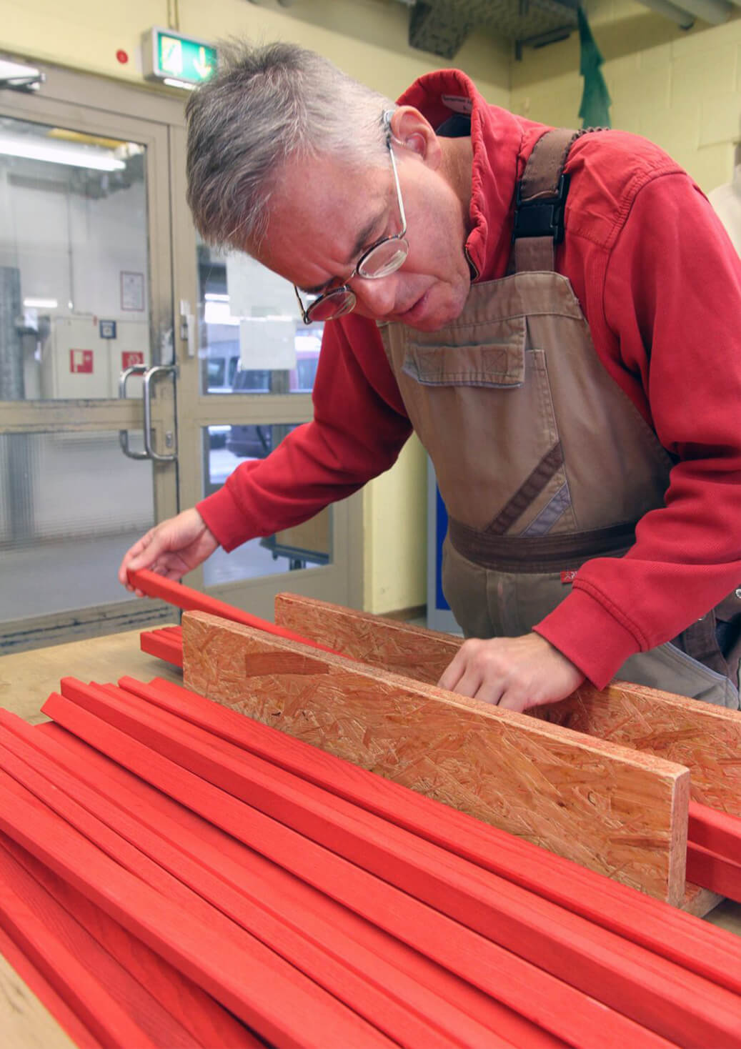 A man wearing an apron inspects red wooden boards that will be crafted into Metalog tools for use in hands on training activities