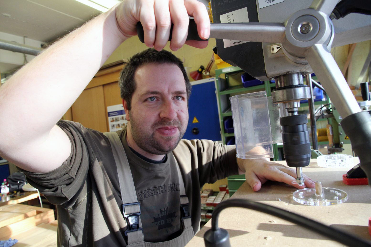 A man wearing an apron uses a drill press to build a training tool for Metalog, a top brand for experiential learning activities