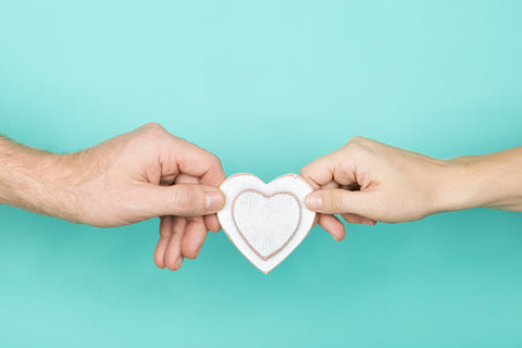 Two hands are holding a cutout paper heart in front of an aqua green background