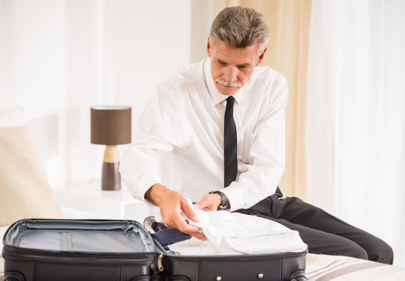 Businessman wearing dress shirt packing his other one in a suitcase for travel