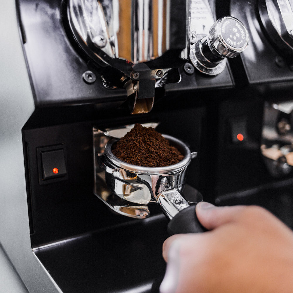 Barista mit kaffeehalter-siebträger mit gemahlenem kaffee in der nähe einer  professionellen espressomaschine
