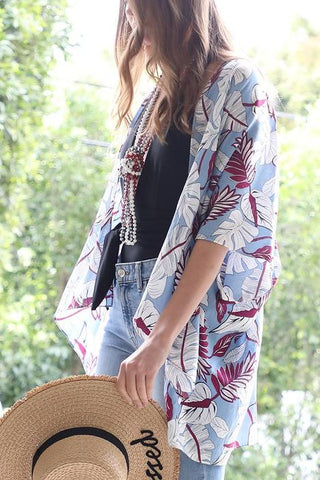 Woman wearing printed kimono and holding a sun hat.