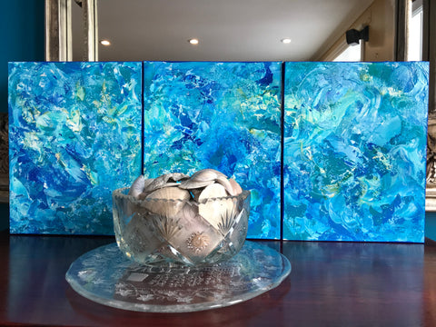 Motion of the Ocean are three , 11x14 abstract paintings arranged behind a bowl of seashells