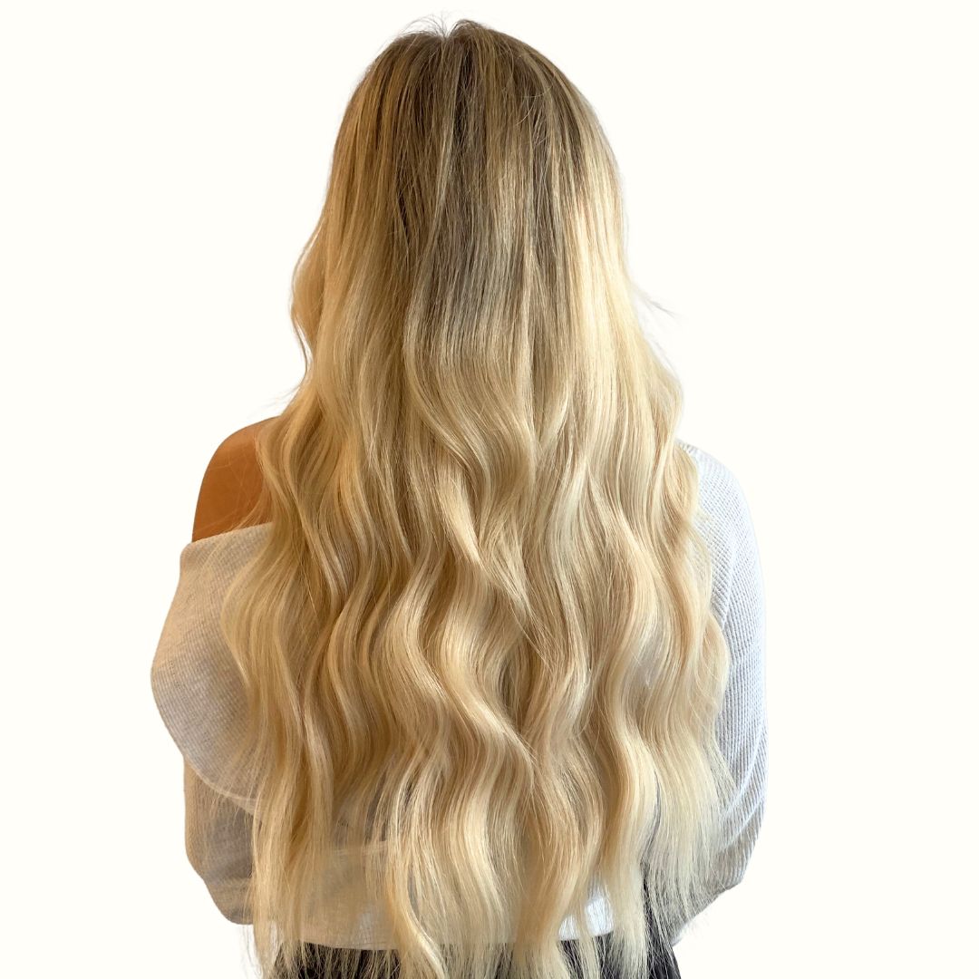 Long, wavy blonde hair viewed from the back against a neutral background.