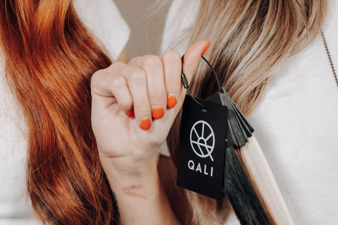 hand holding a color ring with the QALI logo on the front, ginger and blonde hair in the background behind color ring