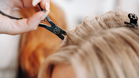 zoomed in shot of black branded QALI pliers working on a warm blonde head of hair
