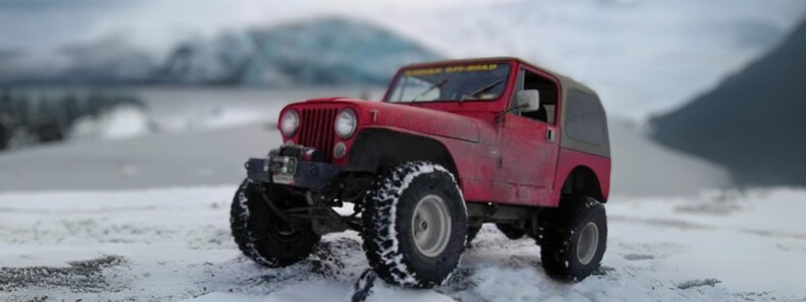A red custom jeep cj5 powers through snowy terrain with a lift, wide tires, and steel bumpers — the kind of upgrades that make old rigs winter-capable.