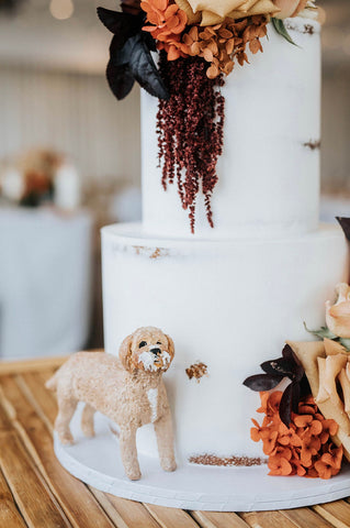 Dog cake topper at the base of a white wedding cake with cake on his face