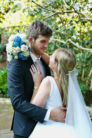 bride and groom looking into each others eyes with a blue bouquet in her arms around his neck