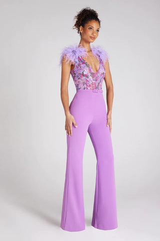 Woman wearing lilac jumpsuit with feather trim on shoulders