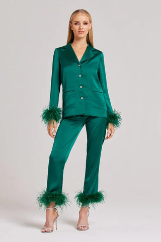 A woman wearing emerald green satin pyjamas with a feather trim cuff.