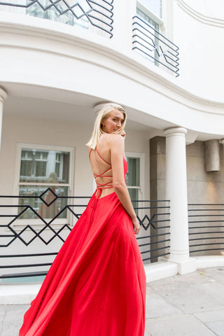 woman stood in red backless dress posing in front of white building with short blonde hair