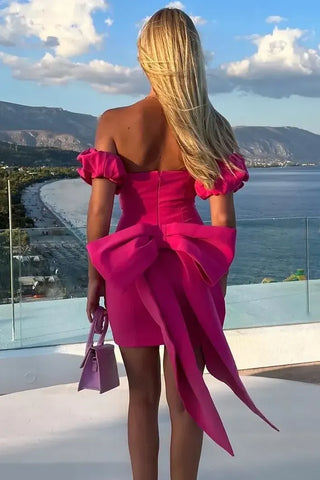 woman with blonde hair stood wearing pink nadine merabi dress holding handbag in her left hand