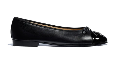 leather black ballet flat shoes with a small heel designed by chanel sat against a white background
