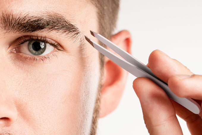 a close-up of a man using tweezers on his eyebrows